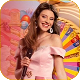 Веселая женщина с микрофоном в розовом платье с открытыми плечами, ведущая игровое шоу с колесом Melbet